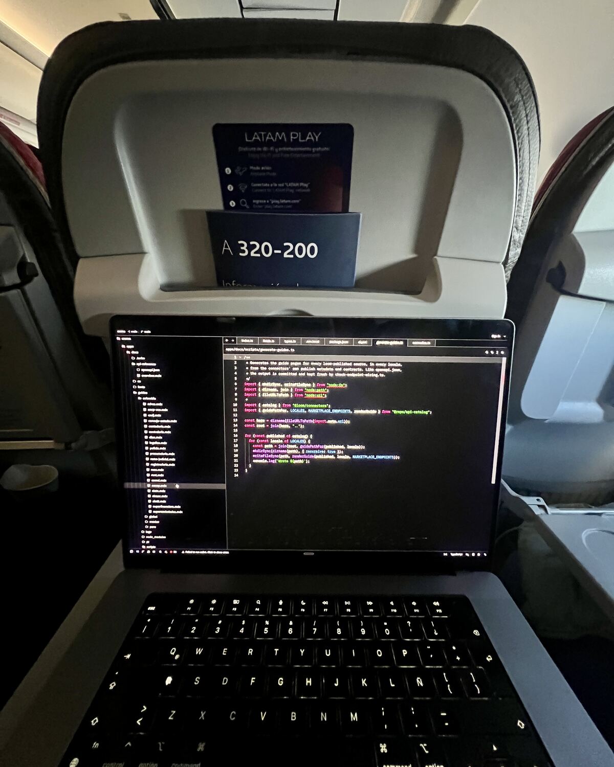 Un portátil abierto sobre la mesa de un avión, código en la pantalla, el respaldo de adelante marcado A320-200